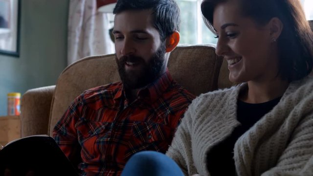 Couple sitting on sofa and reading novel in living room at home