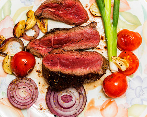 Ribeye steak with blood on a plate with tomatoes, onions, garlic, olive oil 