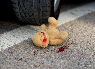 toy bear in the blood under the car wheels
