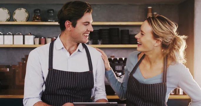 Smiling waiter and waitress using digital tablet while talking to each other in the cafe 4k