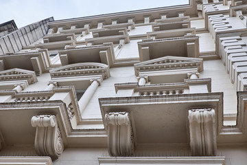 Sections of a plastered facade with elaborate decorations around the windows and balconies of a building in London City