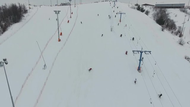 Aerial view: Skiers and snowboarders going down the slope in winter day. Skiers and snowboarders enjoying on slopes of ski resort in winter season. 4K video, aerial footage.