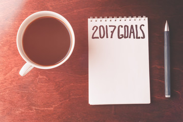 2017 goals list with notebook, cup of coffee on wooden table.