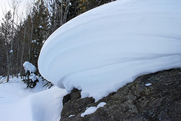 A snow drift sculpted by the wind sits precariously atop a boulder