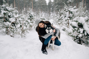 Fototapeta na wymiar Girl stroking Husky dog in winter snowy pine forest