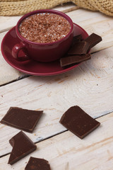 Milk chocolate in a cup on a saucer on a light wooden background