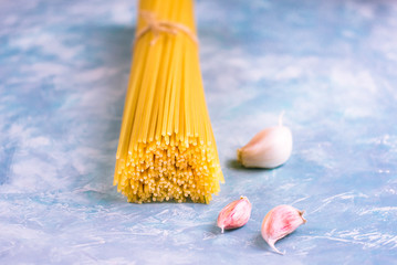 Bundle of uncooked spaghetti tight with twine on blue and white concrete background with scattered pinkish garlic cloves,close up