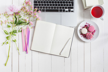 Feminine flat lay workspace with laptop, cup of tea, macarons and flowers on white wooden table....
