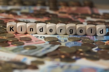kindergeld - Holzwürfel mit Buchstaben im Hintergrund mit Geld, Geldscheine