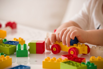 Close up of child's hands playing with colorful plastic bricks at the table. Toddler having fun and building out of bright constructor bricks. Early learning.  stripe background. Developing toys