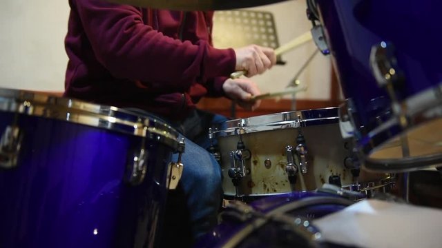 Drummer playing instrument. Closeup on snare tom, movement with musician in background