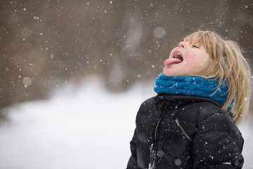 Cute blond kid boy catching snowflakes with his tongue while walking in a winter park. Child having fun with snow outdoors. - 134488371
