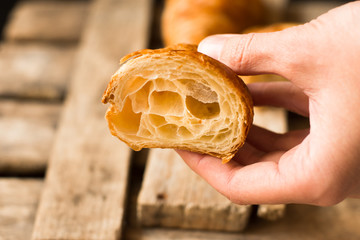 Woman´s hand holding freshly baked croissant cut in half, flaky pastry inside visible, reclaimed barn wood background,minimalistic style,kinfolk