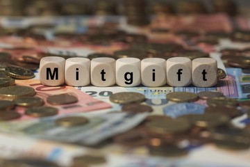 mitgift - Holzwürfel mit Buchstaben im Hintergrund mit Geld, Geldscheine