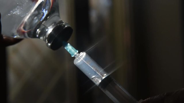 Close up of injection syringe needle filling transparent saline solution from medical bottle