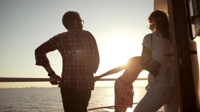 Caucasian family standing near railing looking at sea and sun in slowmotion