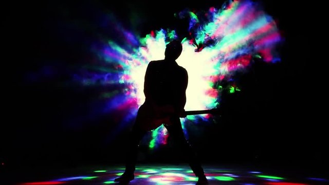 Rock musician, guitarist, showman. Strobe lights, smoke machines. Concert rock band performing on stage with singer performer, guitar, drummer. Music video, heavy metal or rock group. Slow motion. 