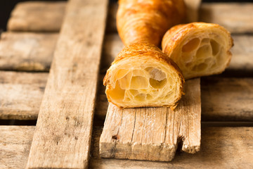 Fresh croissant cut in half with flaky pastry inside visible, on vintage wood background,close up,kinfolk