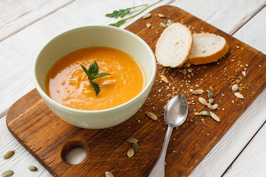 Tasty pumpkin cream-soup with bread and spoon. Top view on orange carrot porridge in bowl on wooden board. Homemade food, vegetarian cuisine, healthy eating concept