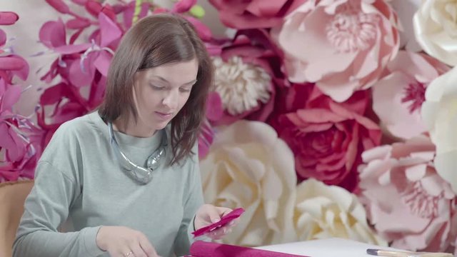 Woman doing art crafts from corrugated paper fuchsia color: a giant wall flower - modern fittings and decoration of wedding ceremonies and parties. Decorator cut colored paper scissors.