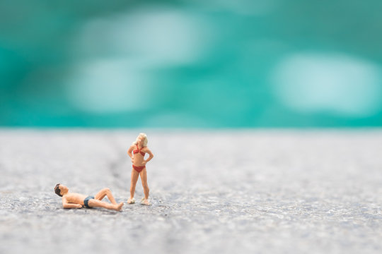 Miniature people in swimsuit relax near swimming pool