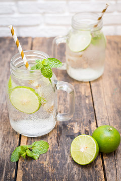 Homemade lemonade drink with fresh lime in glass on old wooden background
