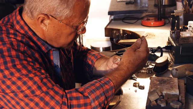 Goldsmith fixing diamond on ring with tweezers in workshop 4k