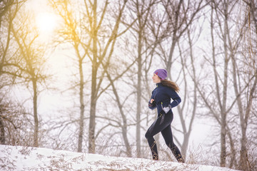 Runner jogging in snow. Young woman fitness model running in a city park