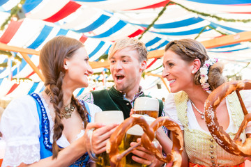 Drei Freunde auf der Dult oder Oktoberfest beißen in Riesenbrezen und trinken Bier im Bierzelt