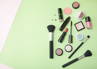 Make up products arranged on a pastel green and pink background, with blank space at side