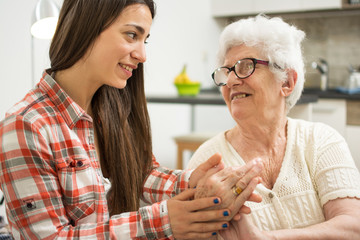 Grandmother and granddaughter sitting on couch and holding hands of each other.