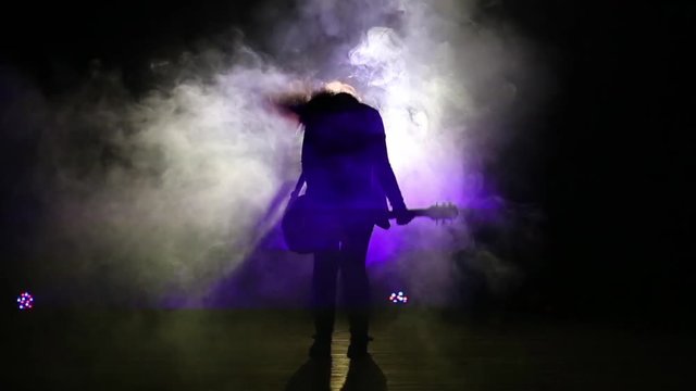 Silhouette of a girl with a guitar plays hard rock. Rock concert, guitarist playing on stage. Music video punk, heavy metal.