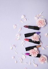 Assorted lipstick make up and flowers arranged on a pastel purple background with empty space at side