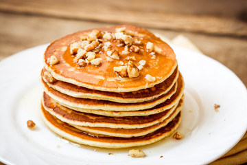 Pancakes with honey and walnuts on rustic wooden background