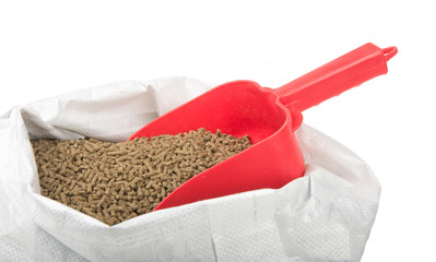 Red scoop inserted in a bagful of pelleted horse feed, isolated on white