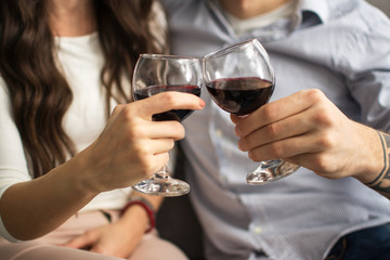 Close up of hands of young loving couple clinking glasses of red wine.