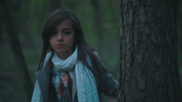 Little European brunette girl in a stylish look. Frightened lonely girl is wondering in the dark forest, she looks around and moving forward in the forest. Fearful atmosphere.