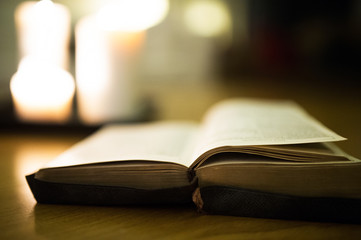 Bible laid on wooden floor, burning candles in the background