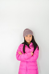 Happy Asian girl wearing pink down jacket sitting on gray backgr
