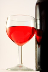 Bottle and glass with red wine on a light background