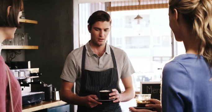Smiling waiter serving cup of coffee to women at cafe counter 4k