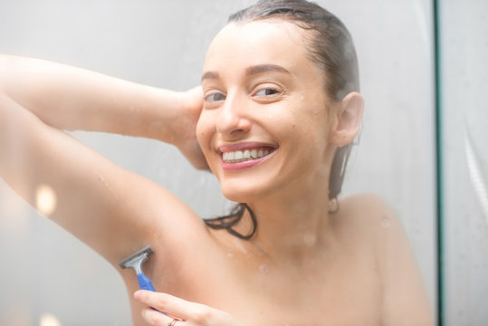 Young smiling woman shaving armpits in the shower