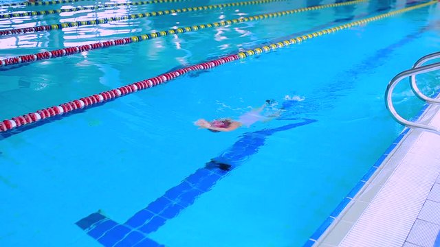 Little girl in goggles swimming breaststroke in a blue pool