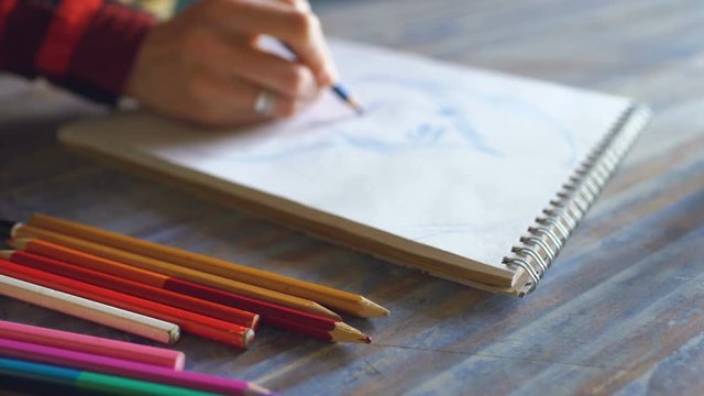 Young woman artist painting scetch on paper notebook with pencil closeup