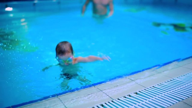 The father teaches his little son to swim in the blue swimming pool
