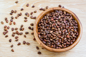 Кедровые орехи в деревянной тарелке и рассыпанные на столе