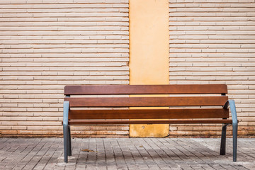 Wood bench on a city street with brick wall behind 