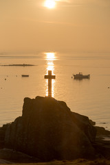 Kreuz in Reflexen der aufgehenden Sonne auf dem Meer, Bretagne, Frankreich