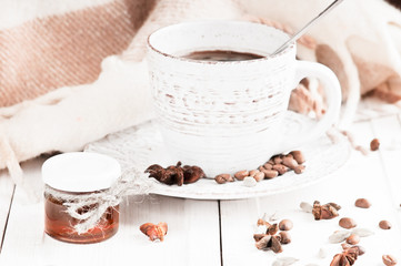 vintage mug with hot coffee and spices decorated with a blanket in cage on a white wooden surface