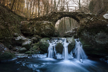 Naklejka na ściany i meble Frozen waterfall under old stone bridge